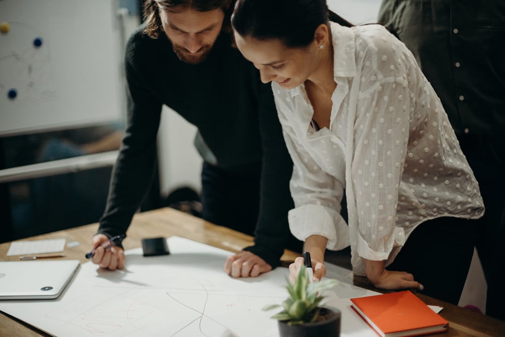 man-and-woman-leaning-on-table-staring-at-white-board-on-top-3205570